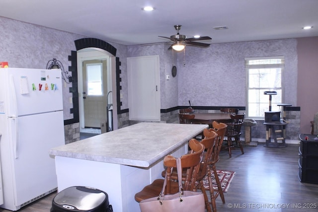 kitchen with ceiling fan, arched walkways, light countertops, freestanding refrigerator, and dark wood-style floors