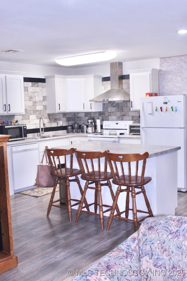 1005 N Osage St, Chouteau, OK 74337 - kitchen featuring wall chimney exhaust hood, white appliances, a sink, backsplash, and a breakfast bar area