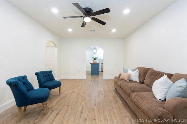 living area featuring visible vents, arched walkways, baseboards, and light wood finished floors
