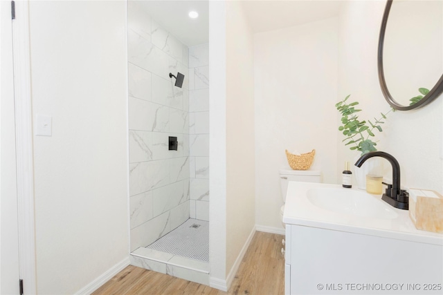full bath with vanity, baseboards, a tile shower, and wood finished floors