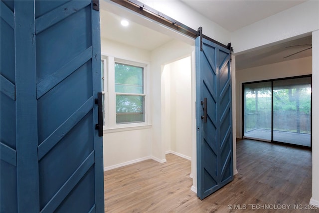 interior space featuring baseboards, a barn door, light wood-style flooring, and a wealth of natural light