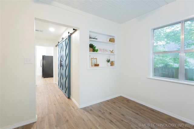 hallway featuring light wood-type flooring, a barn door, and baseboards