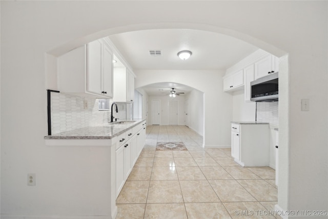kitchen featuring white cabinets, a sink, arched walkways, a ceiling fan, and stainless steel microwave