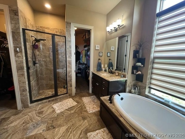full bathroom featuring vanity, a walk in closet, a garden tub, and a stall shower