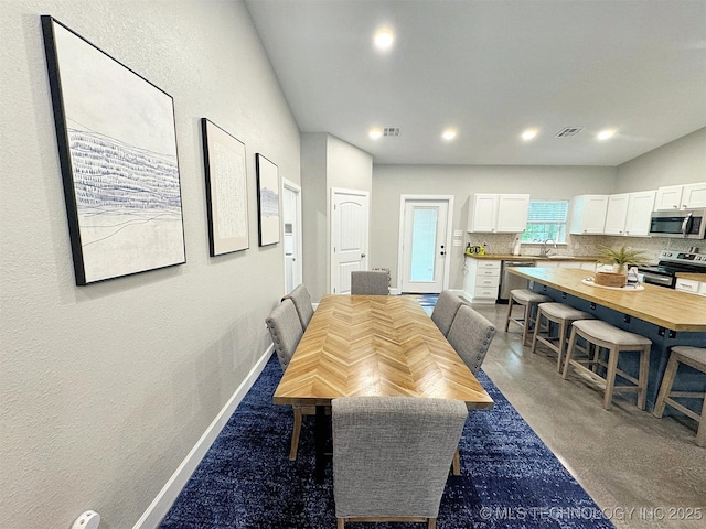 dining room with baseboards, a textured wall, finished concrete floors, and visible vents
