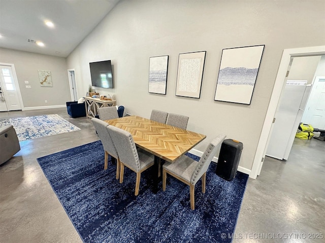 dining space featuring finished concrete floors, baseboards, and high vaulted ceiling