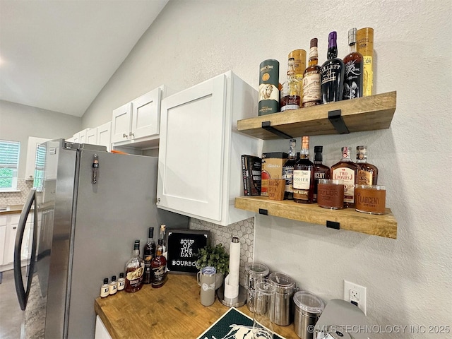 interior space with tasteful backsplash, open shelves, vaulted ceiling, white cabinets, and a textured wall
