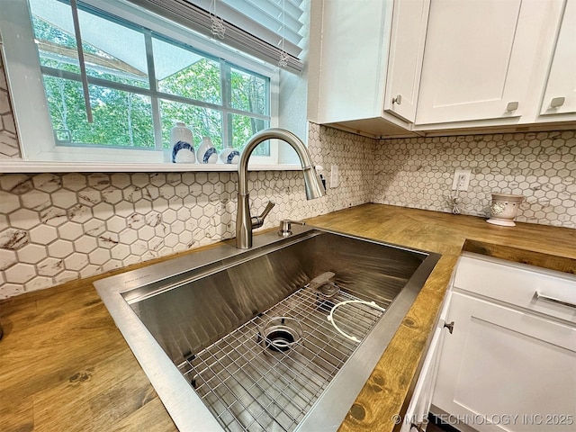 room details with backsplash, white cabinetry, butcher block counters, and a sink