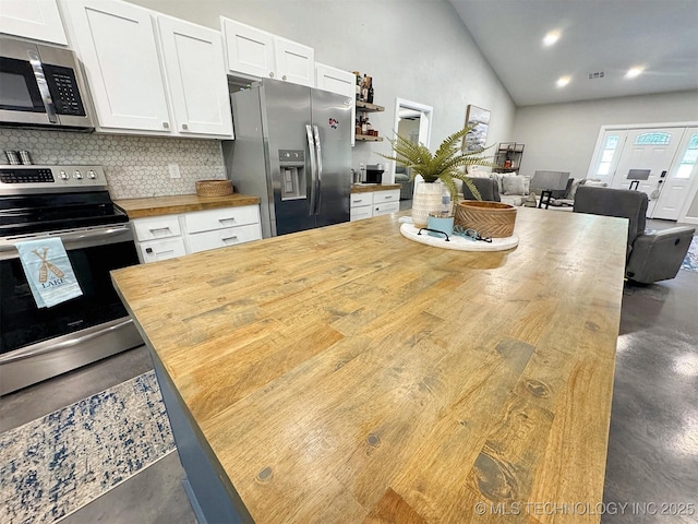 kitchen with white cabinets, stainless steel appliances, finished concrete floors, tasteful backsplash, and butcher block counters