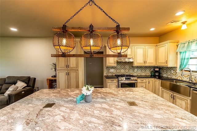 kitchen with cream cabinets, a sink, stainless steel range with gas cooktop, under cabinet range hood, and visible vents