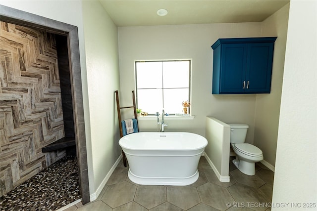 bathroom featuring toilet, tile patterned floors, a freestanding tub, baseboards, and tiled shower