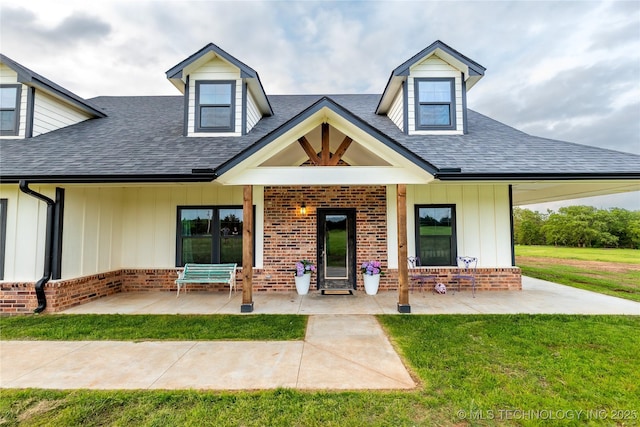 view of front of property featuring a shingled roof, board and batten siding, brick siding, and a front yard