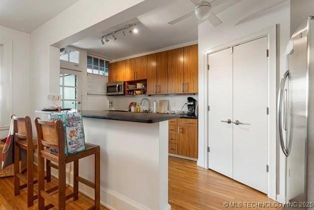 kitchen with brown cabinetry, dark countertops, rail lighting, light wood-style flooring, and appliances with stainless steel finishes