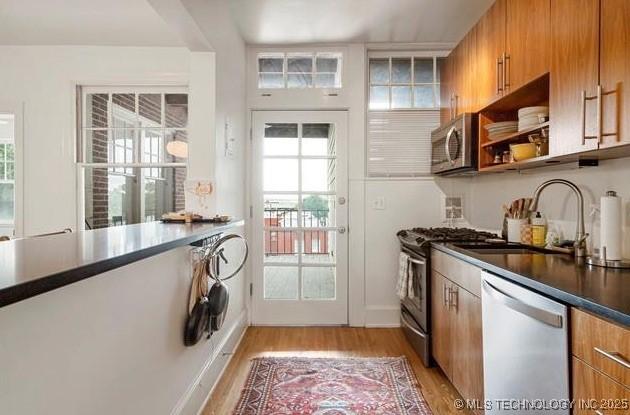 kitchen with appliances with stainless steel finishes, brown cabinetry, a healthy amount of sunlight, and light wood finished floors