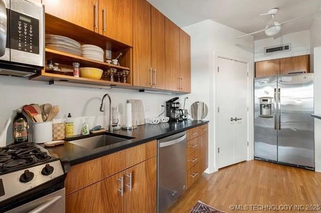 kitchen featuring visible vents, dark countertops, light wood-type flooring, a sink, and stainless steel appliances