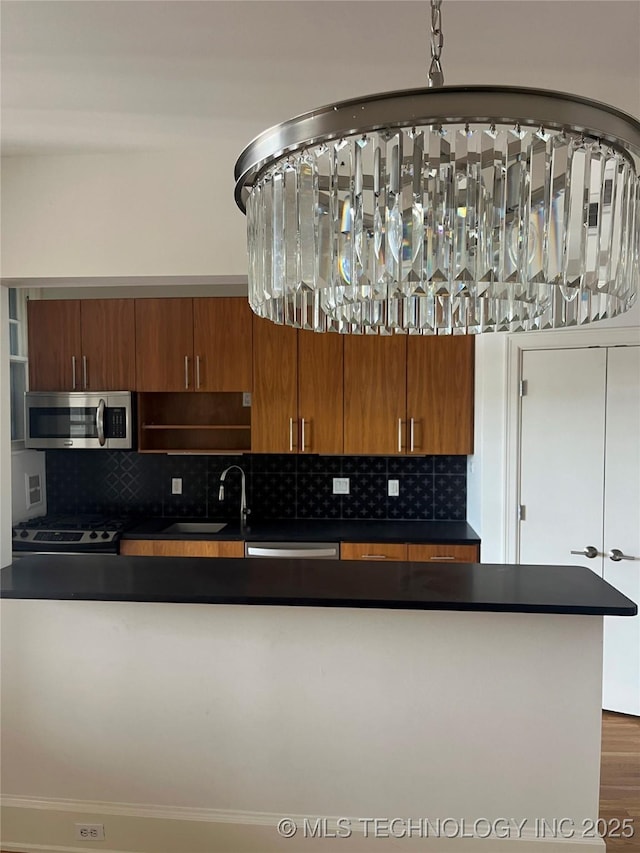 kitchen featuring stainless steel microwave, dark countertops, a sink, and brown cabinetry
