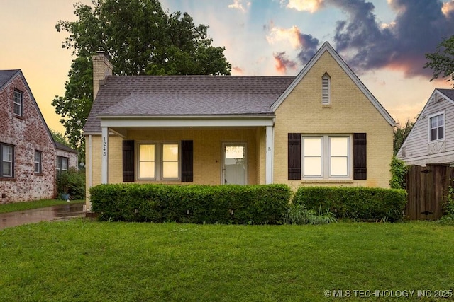 view of front of house with fence, a chimney, brick siding, and a front yard