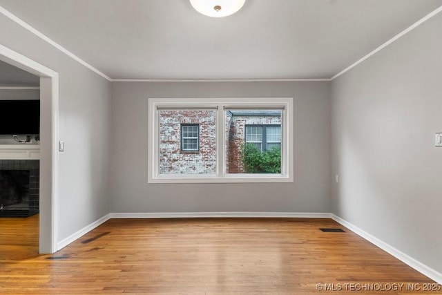 spare room featuring crown molding, light wood finished floors, visible vents, and a fireplace