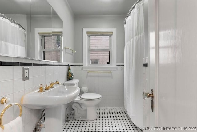 full bathroom featuring toilet, tile patterned floors, a shower with shower curtain, a wainscoted wall, and tile walls