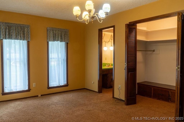 unfurnished bedroom with an inviting chandelier, a closet, a textured ceiling, carpet flooring, and ensuite bath