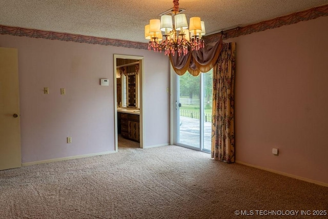 carpeted empty room featuring a textured ceiling, an inviting chandelier, and baseboards