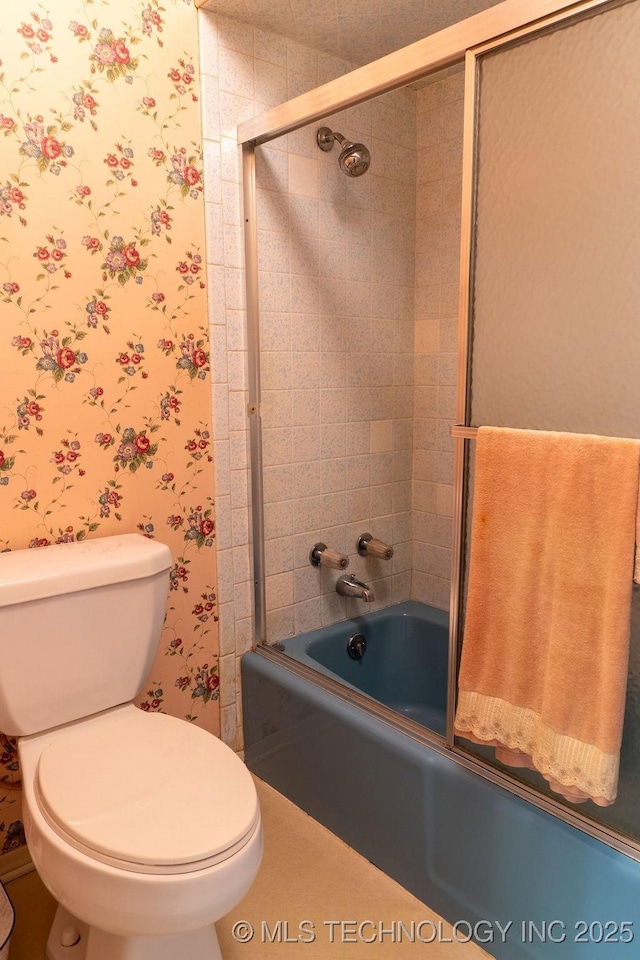 bathroom featuring combined bath / shower with glass door, toilet, and wallpapered walls