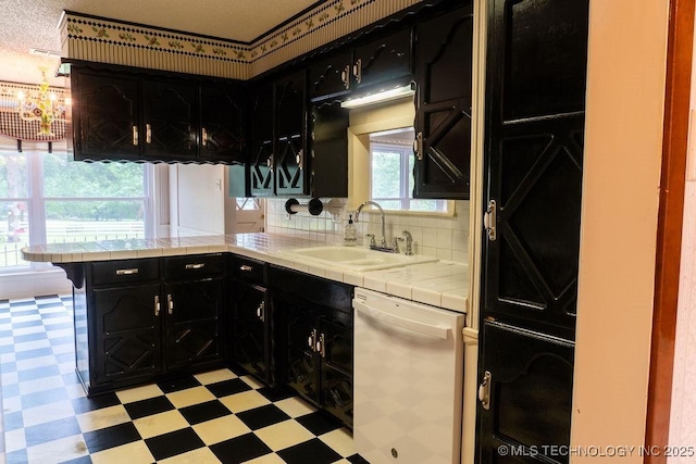 kitchen with tile countertops, dishwasher, a sink, dark cabinets, and light floors