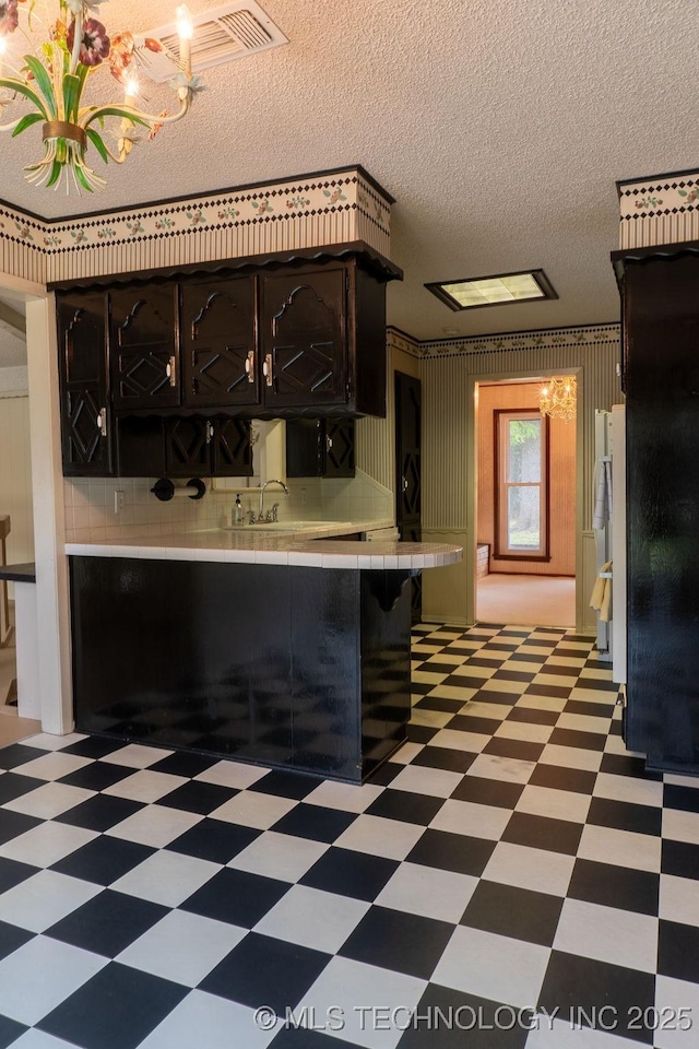 kitchen with tile counters, a textured ceiling, an inviting chandelier, and light floors