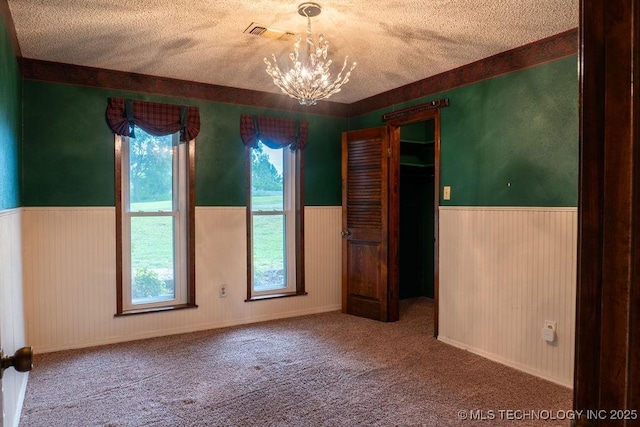 empty room with carpet flooring, a notable chandelier, wainscoting, a textured ceiling, and visible vents