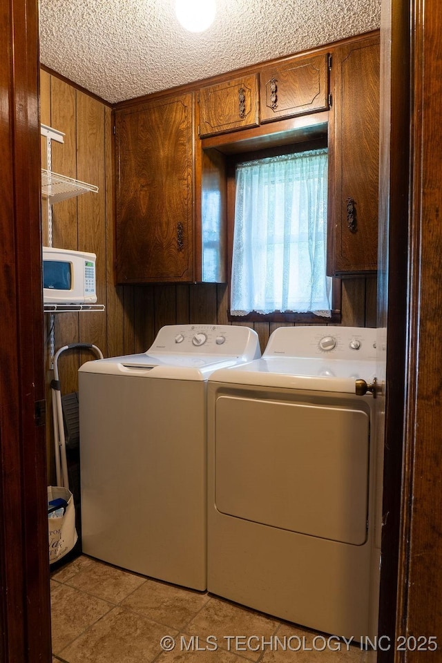 washroom with a textured ceiling, cabinet space, wooden walls, light tile patterned flooring, and washer and clothes dryer