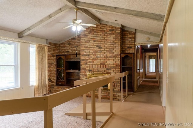 unfurnished living room featuring ceiling fan, brick wall, a textured ceiling, vaulted ceiling with beams, and carpet