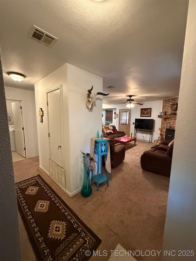 carpeted living area featuring a textured ceiling, a ceiling fan, a brick fireplace, and visible vents