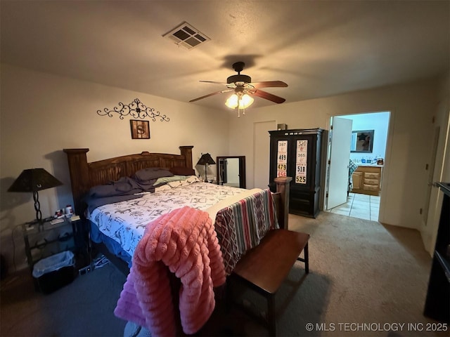 bedroom with ensuite bathroom, a ceiling fan, light colored carpet, and visible vents