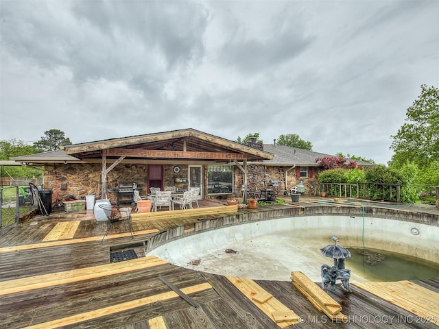 rear view of property with a deck, outdoor dining space, and stone siding