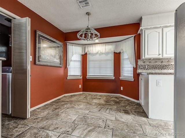 unfurnished dining area featuring visible vents, a textured ceiling, baseboards, and a notable chandelier