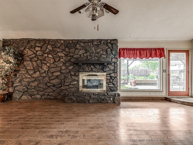 unfurnished living room featuring a fireplace, a textured ceiling, ceiling fan, and wood finished floors