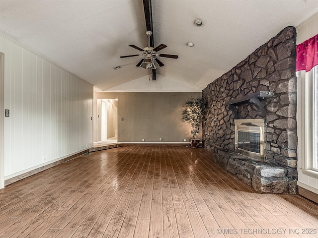 unfurnished living room with a fireplace, a textured ceiling, a ceiling fan, vaulted ceiling with beams, and hardwood / wood-style flooring