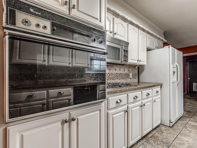 kitchen with white refrigerator with ice dispenser, gas cooktop, stainless steel microwave, white cabinets, and tasteful backsplash