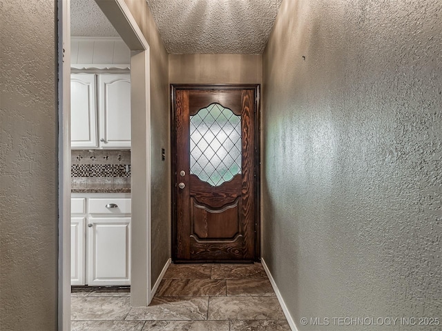 entryway featuring a textured ceiling, a textured wall, and baseboards