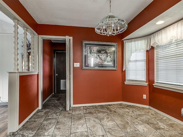 unfurnished dining area with a textured ceiling, a notable chandelier, and baseboards