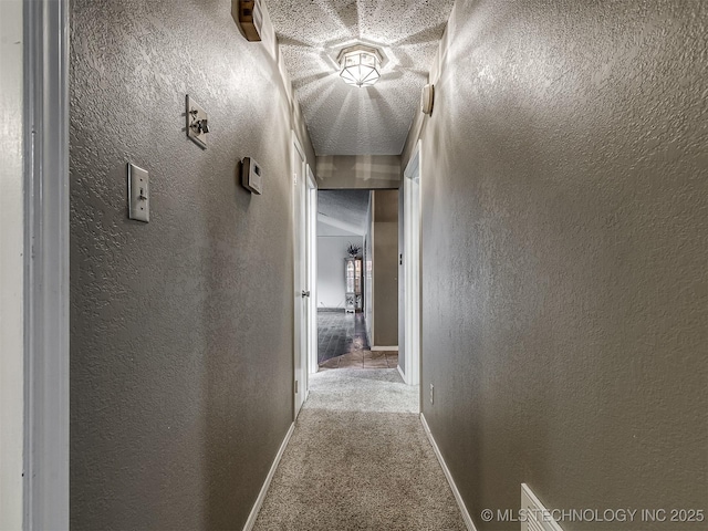 hallway featuring a textured wall, baseboards, and carpet