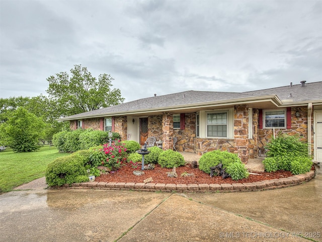 single story home with roof with shingles, a front yard, a porch, and stone siding
