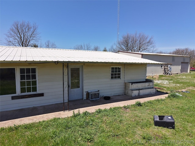 back of property featuring a lawn, a patio, and metal roof