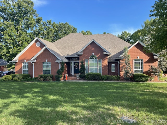 view of front of house featuring brick siding, a front yard, and roof with shingles