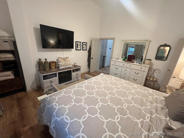 bedroom with baseboards, high vaulted ceiling, and wood finished floors