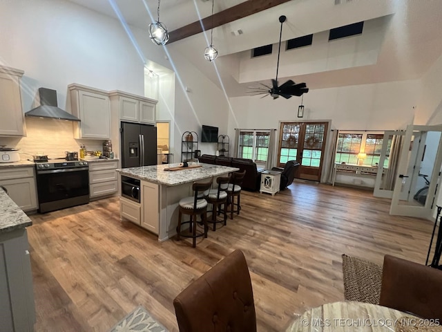 kitchen with wall chimney range hood, electric range, black fridge, high vaulted ceiling, and open floor plan