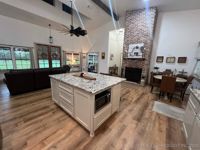 kitchen featuring built in microwave, wood finished floors, high vaulted ceiling, open floor plan, and white cabinetry