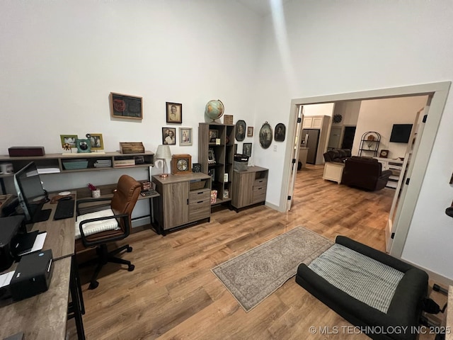 office space featuring baseboards, a towering ceiling, and wood finished floors
