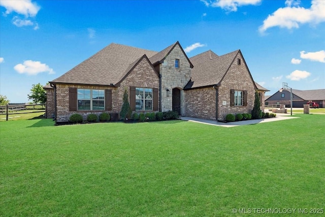 french country home with brick siding, fence, a front yard, and roof with shingles