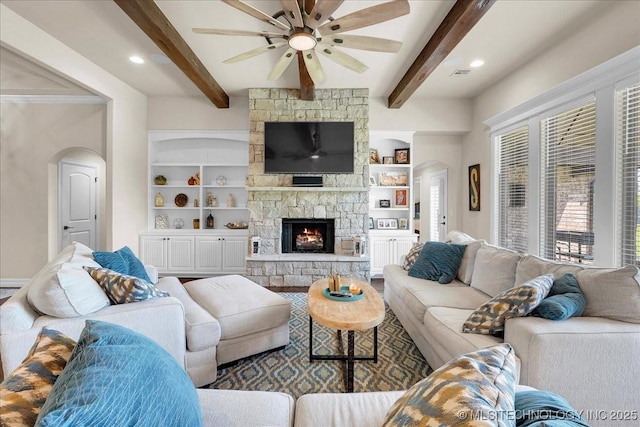 living room featuring ceiling fan, visible vents, arched walkways, a fireplace, and beam ceiling
